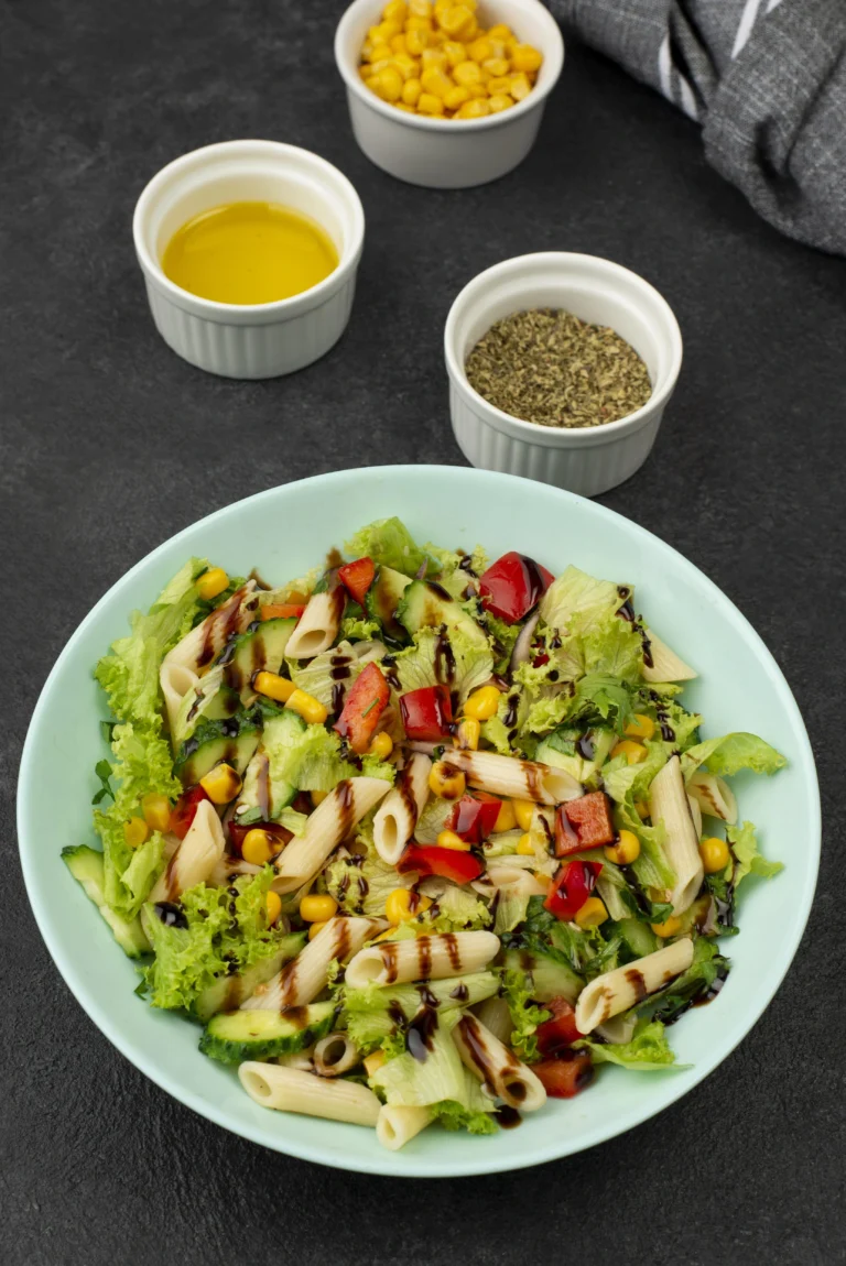 A pasta salad with penne, fresh vegetables, and balsamic drizzle, surrounded by small bowls of oil and herbs. Not an elote salad.